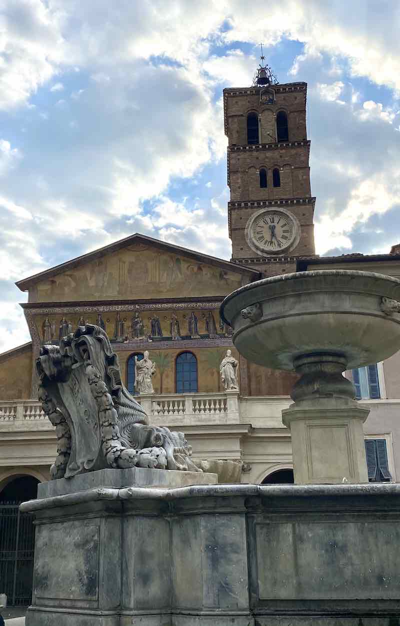 Architettura storica a Roma, chiesa e fontana in piazza, torre con orologio, monumento in marmo, cielo nuvoloso, dettagli artistici e simbolici, cattedrale e piazza principale.