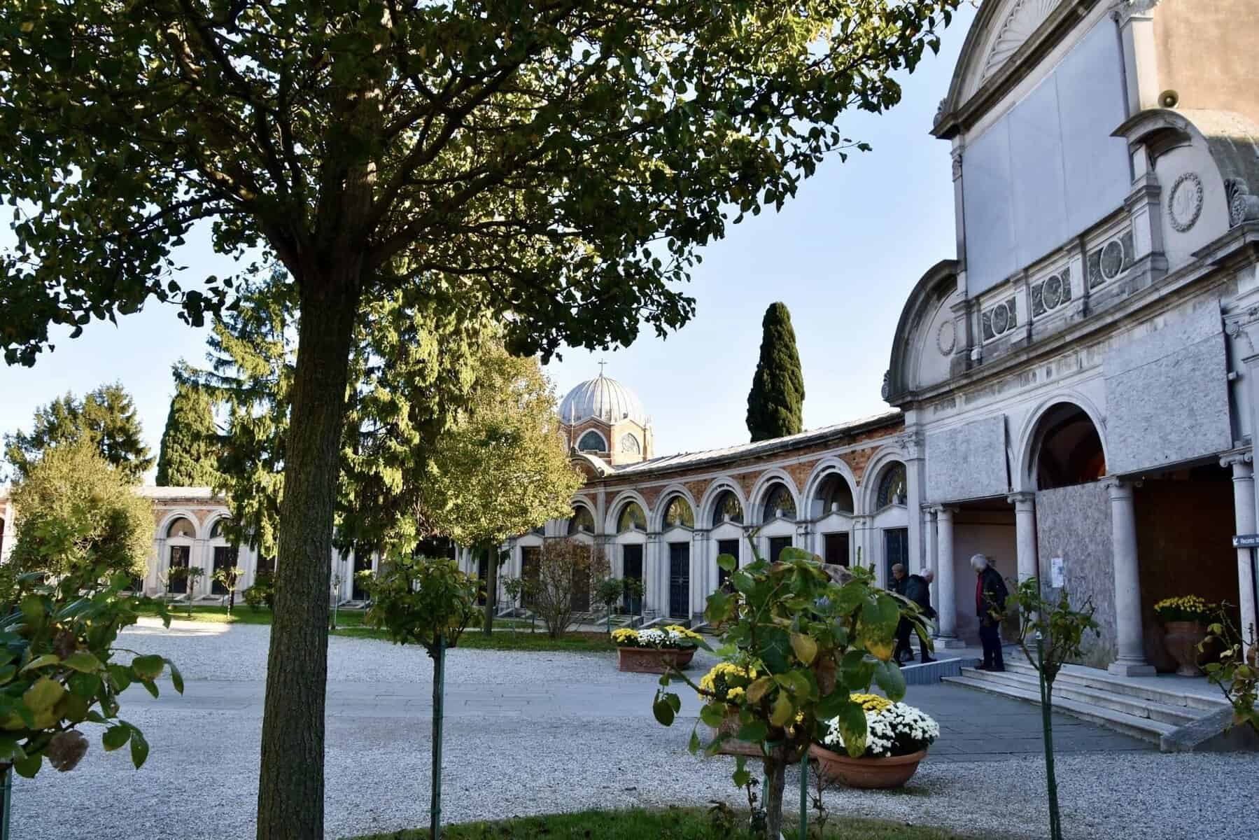 Cimitero di San Michele. Cortile di un edificio storico con alberi e piante, chiesa con cupola sullo sfondo, ambiente tranquillo e suggestivo, ideale per turismo culturale e visita religiosa, in Italia.