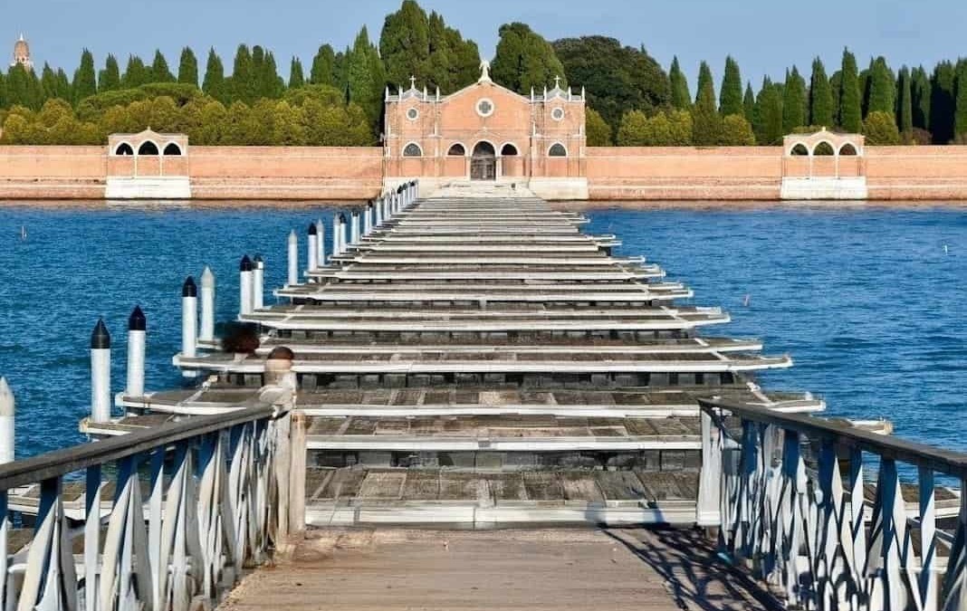 Silenzioso ponte su barche con imbarcadero in legno che conduce a un edificio storico, circondata da acque calme e giardini rigogliosi.