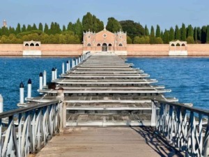 Silenzioso ponte su barche con imbarcadero in legno che conduce a un edificio storico, circondata da acque calme e giardini rigogliosi.