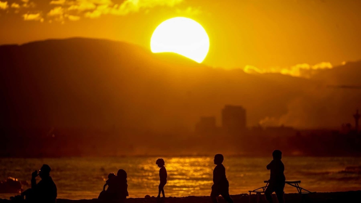 Tramonto dorato sul mare con silhouette di persone che rilassano sulla spiaggia, creando un'immagine suggestiva e perfetta per contenuti di lifestyle e viaggi.