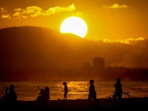 Tramonto dorato sul mare con silhouette di persone che rilassano sulla spiaggia, creando un'immagine suggestiva e perfetta per contenuti di lifestyle e viaggi.