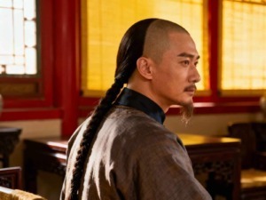 Sorgente di un personaggio con acconciatura tradizionale, in un ambiente storico di legno e feltro, caratteristiche per un contesto culturale orientale o cinematografico.