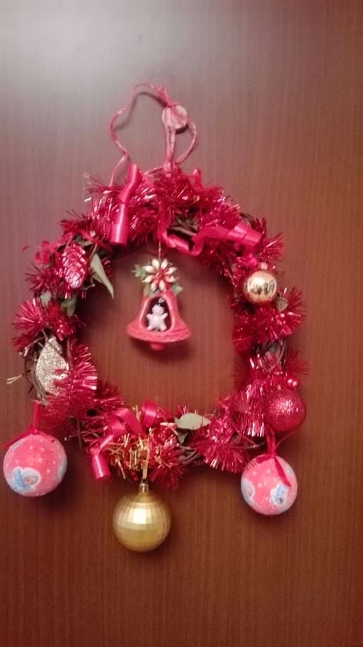 Corona natalizia rossa decorativa con ornamenti colorati, campana dorata e elementi festivi, perfetta per decorare la porta o la casa durante le festività natalizie.