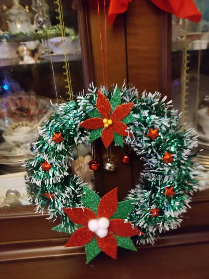 Corona di Natale decorata con fiori di poinsettia, pigne e stelle di tessuto verde e rosso, perfetta per addobbare la porta o la casa durante le festività natalizie.