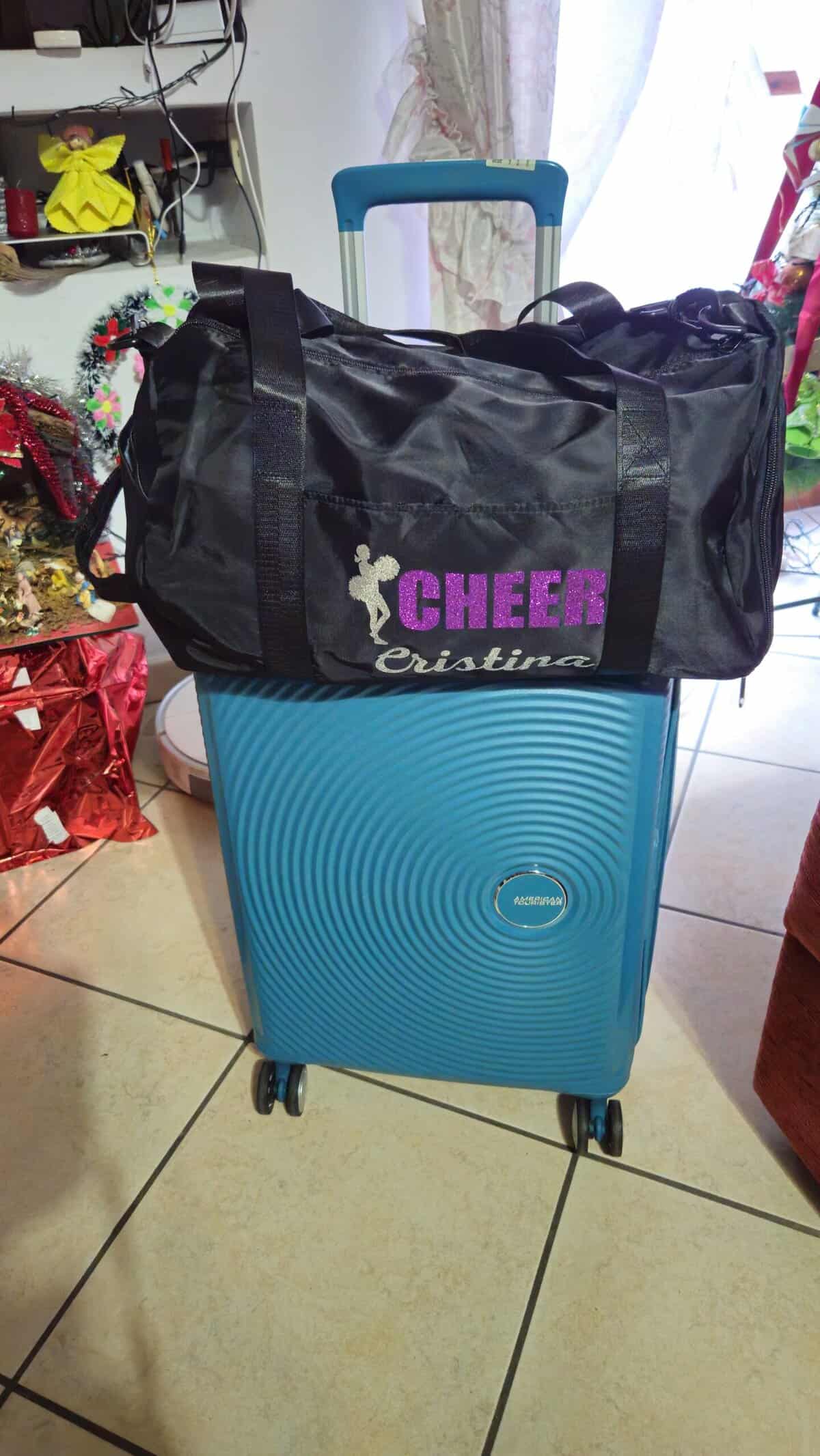 Valigia blu con ruote e dettagli moderni, pronta per il viaggio, con una borsa di cheerleader sopra.