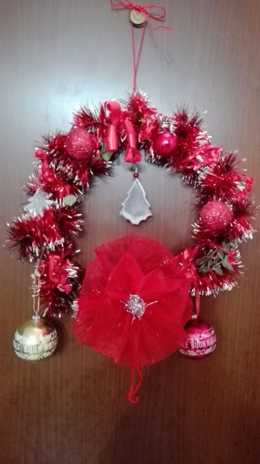 Ghirlanda natalizia rossa decorata con palline, fiocchi e ornamenti per festeggiare il Natale. Perfetta per decorare porte e pareti durante le festività.