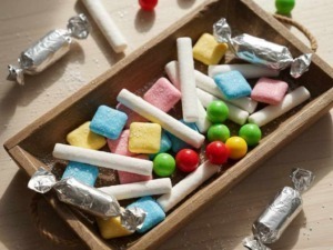 Caramelle colorate di zucchero in una scatola di legno, alcune avvolte in carta argentata, altre non confezionate, con zucchero sparso intorno.