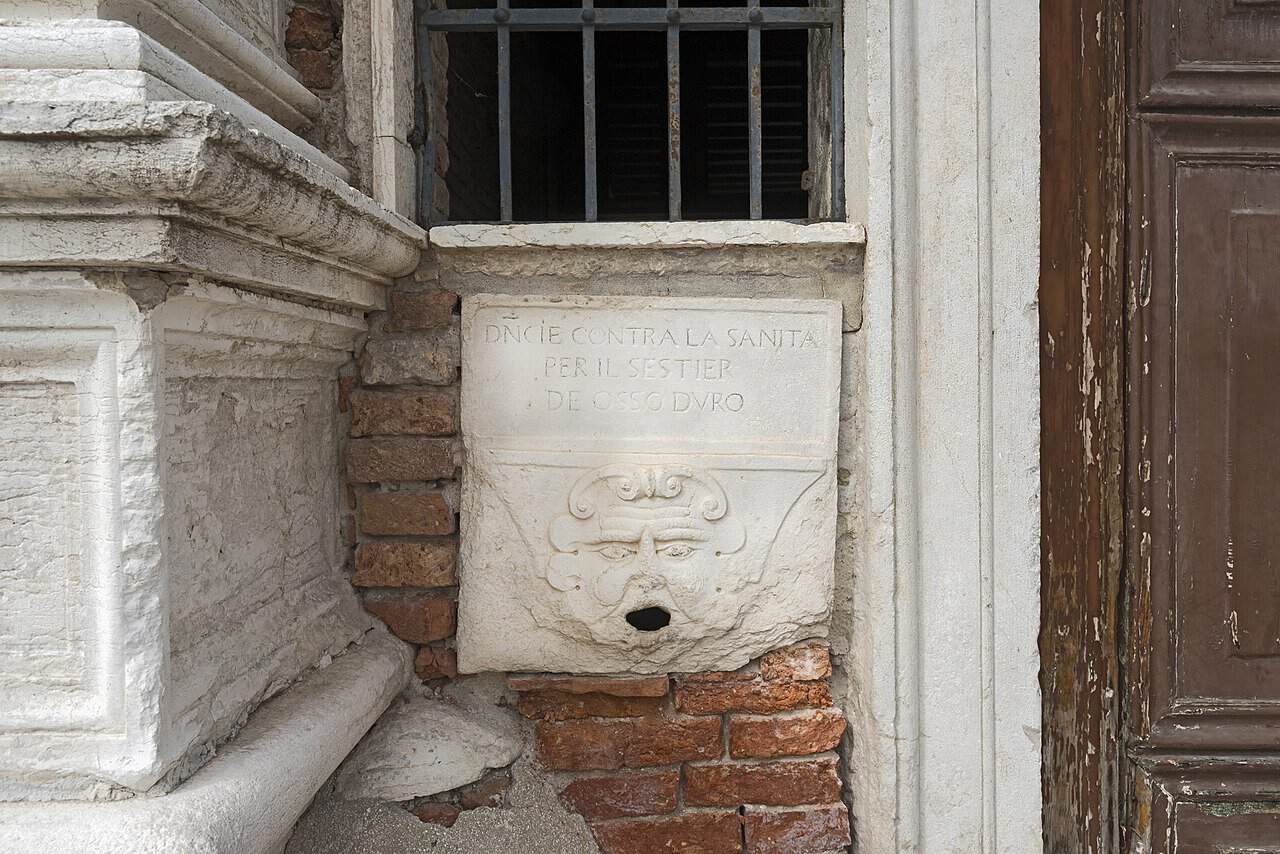 Fonte storica in pietra con iscrizione dedicata alla Santa per il Sestier del Oro, situata su un edificio antico con dettagli in mattoni e pietra.
