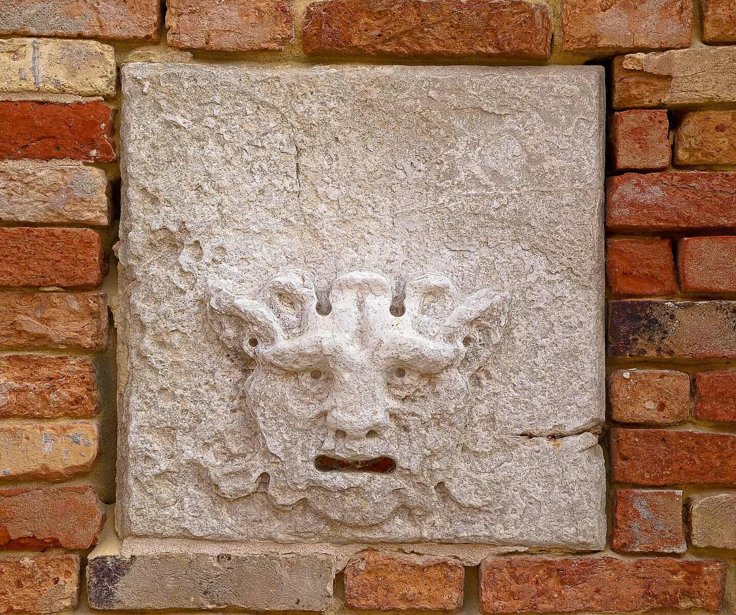 Testo 2: Maschera in pietra con volto di drago scolpita, inserita in un muro di mattoni rossi, decorativa e artistica, perfetta per appassionati di arte e architettura storica.