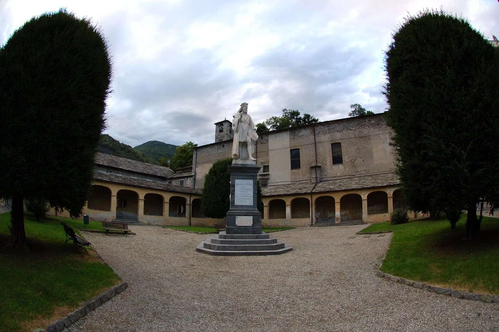 Statua storica nel cortile di un edificio storico con alberi e cielo nuvoloso.