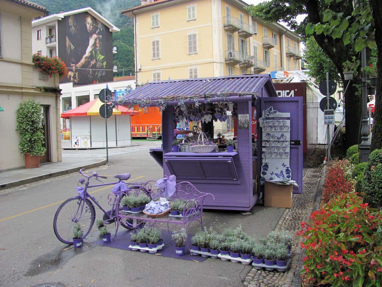 Chiosco di fiori e piante a Varallo Sesia, con biciclette e arredi viola, ideale per scoprire le attrazioni locali e godere della natura e del paesaggio circostante.
