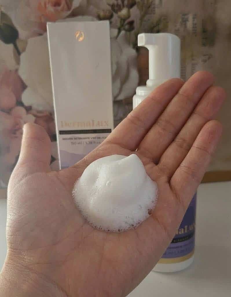 Mano con schiuma di un prodotto cosmetico, con flacone e confezione sullo sfondo, focus sulla cura della pelle e prodotti skincare.