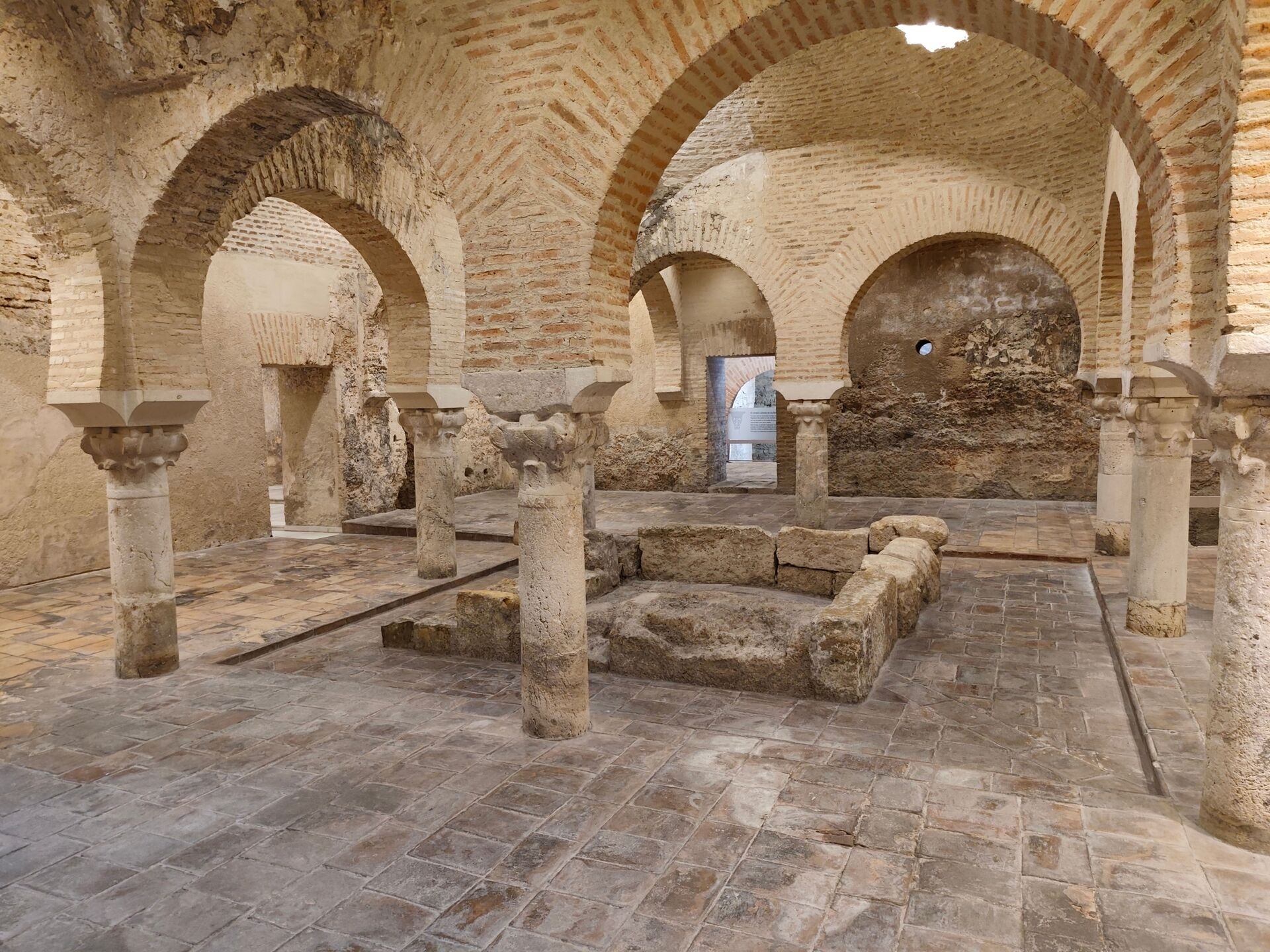 Resti di un edificio storico con archi in mattoni e colonne di pietra, pavimento in pietra e pareti in pietra e mattoni, ambiente interno di un sito archeologico.