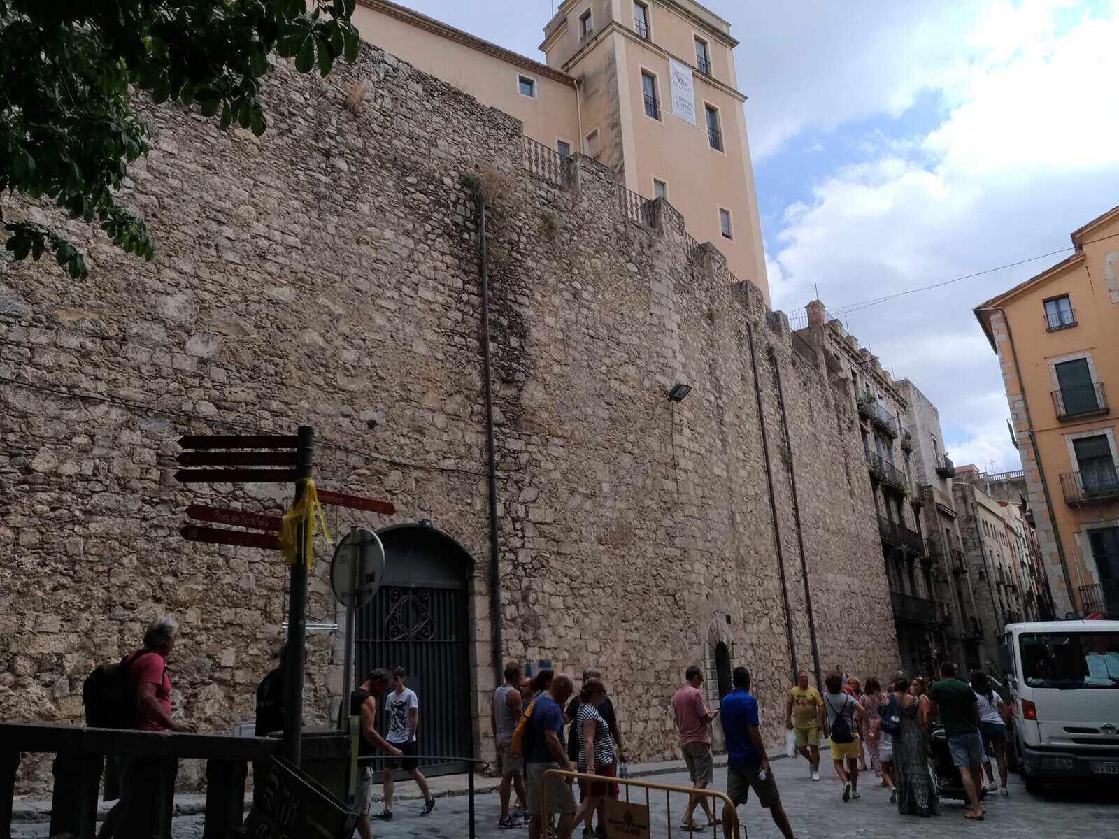 Cosa vedere a Girona in un giorno 7 Gruppo di turisti che passeggia vicino alle antiche mura, con edifici storici sullo sfondo e un cielo nuvoloso