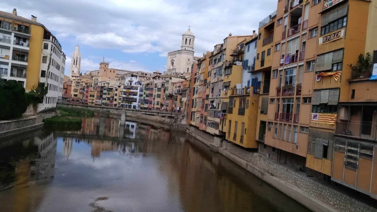 Vista panoramica di Girona con il fiume Onyar e edifici colorati lungo le rive, con chiese storiche sullo sfondo.