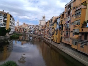 Vista panoramica di Girona con il fiume Onyar e edifici colorati lungo le rive, con chiese storiche sullo sfondo.