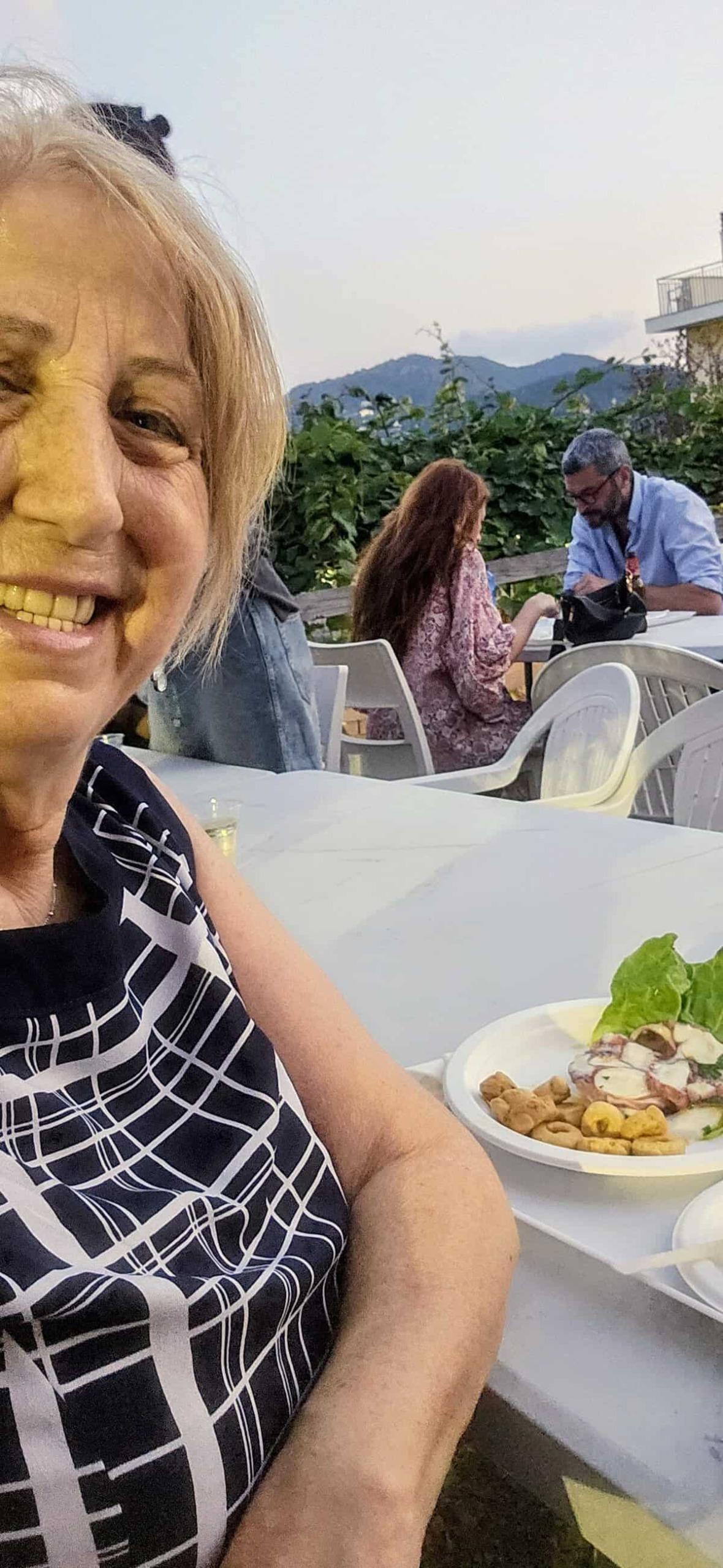 Persone che cenano all'aperto con vista sulle montagne al tramonto, atmosfera rilassante e conviviale.