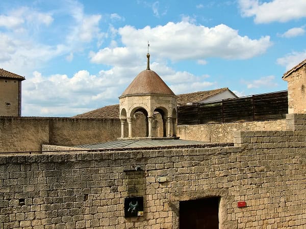 Girona e Game of Thrones: Mappa e Itinerario A Piedi tra le Location della Serie 8 Vista di un'antica torretta in pietra con tetto conico, parte di un forte storico, sotto un cielo azzurro con nuvole.