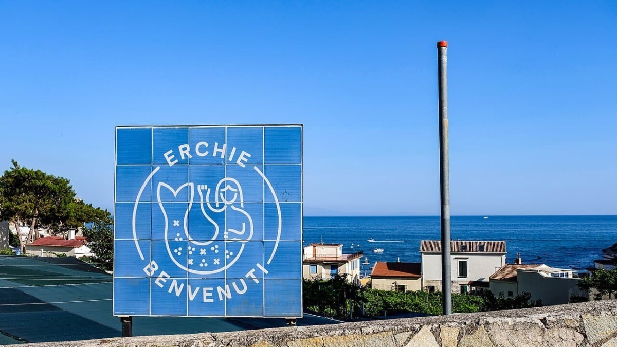 Segnale di benvenuto a Erchie con vista sul mare e case colorate, in una giornata soleggiata e serena.