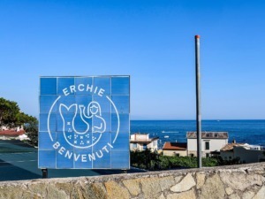 Segnale di benvenuto a Erchie con vista sul mare e case colorate, in una giornata soleggiata e serena.